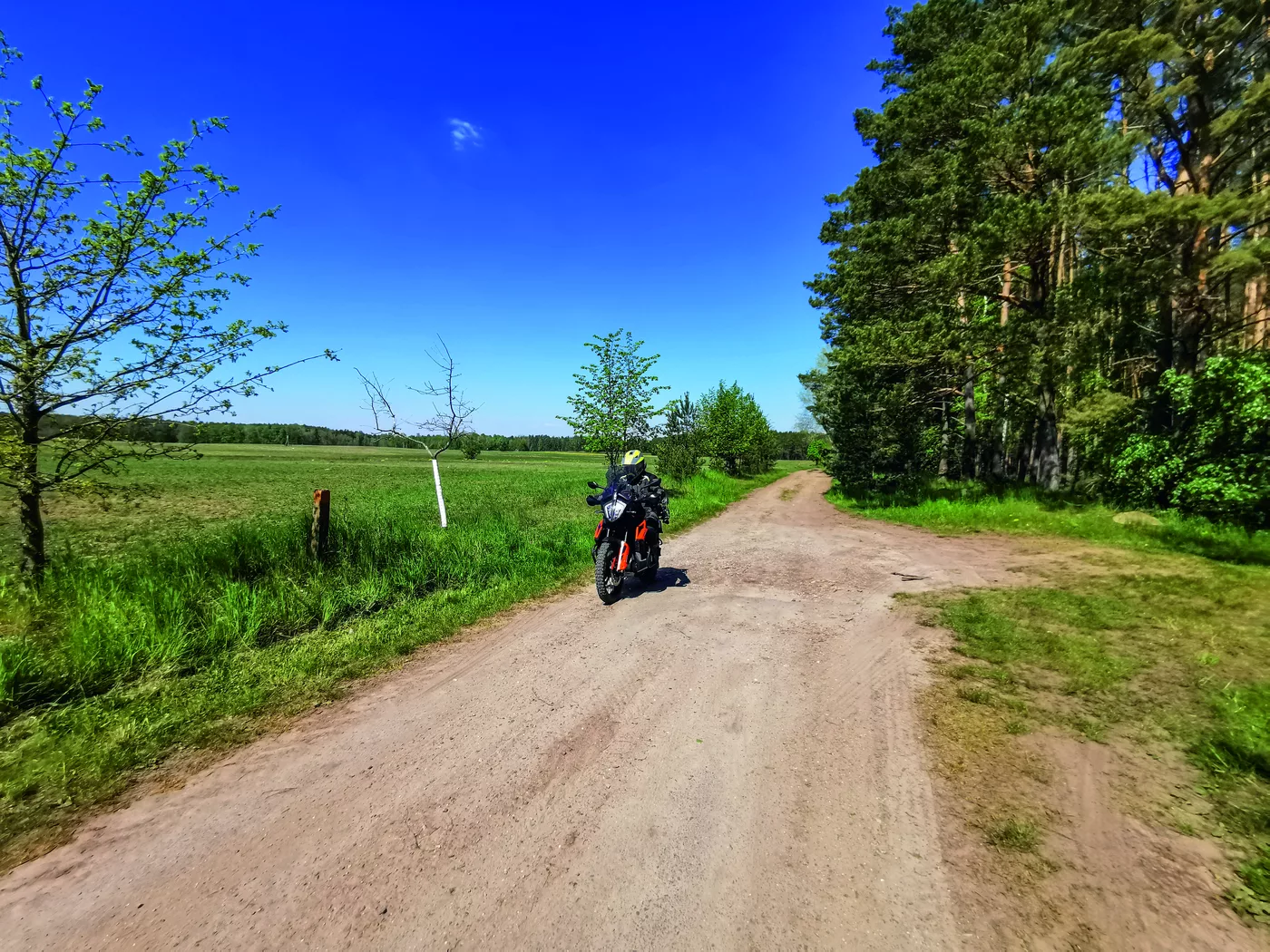 Motorrad auf einem sandigen Feldweg zwischen Wiesen und Waldrand Motorrad auf einem sandigen Feldweg zwischen Wiesen und Waldrand